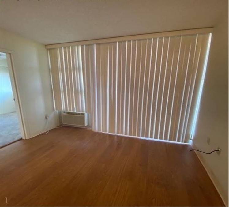 A room with wooden floors and a window covered with vertical blinds.